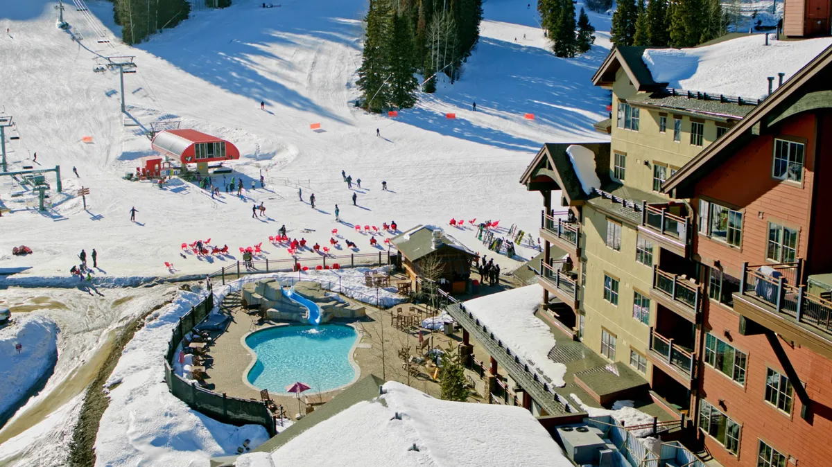 An exterior view combining active ski slopes with an outdoor pool, visible skiers and snowboarders, and the welcoming lodge. There's a lively, joyful energy as guests enjoy both the snow and après-ski amenities, capturing the vibrant community atmosphere of Purgatory Village.