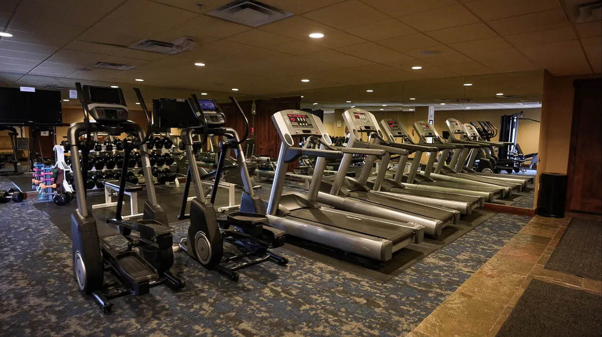 A bright, modern fitness center filled with treadmills, ellipticals, free weights, and exercise mats, all reflected in a mirrored wall. The space feels active and energizing, ideal for guests looking to keep up with workout routines during their stay.
