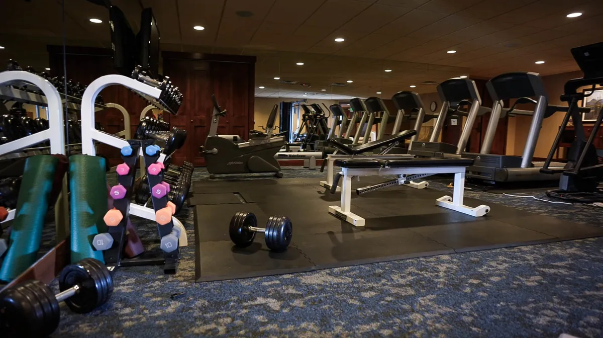 A fully equipped, modern fitness center featuring dumbbells, treadmills, exercise mats, and benches. The mood is energetic, with ample space and equipment for guests to pursue personal fitness goals or join group classes.
