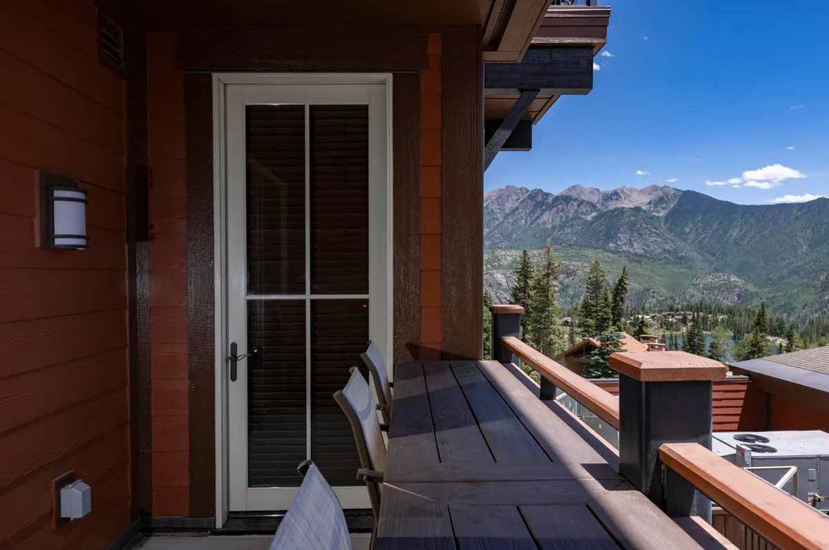 A private balcony with comfortable seating overlooks a breathtaking mountain landscape. The doorway connects seamlessly to the interior, and the tranquil setting invites relaxation with coffee or evening drinks.