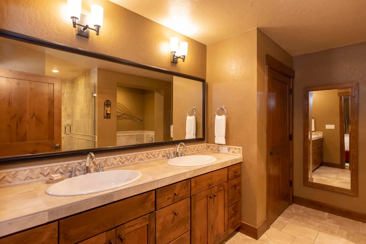 A modern bathroom with double vanity sinks, large mirrors, wooden cabinetry, and towel racks. The space is bright and organized, suggesting enough room for multiple guests to get ready comfortably. The calming decor enhances the sense of a spa-like retreat.