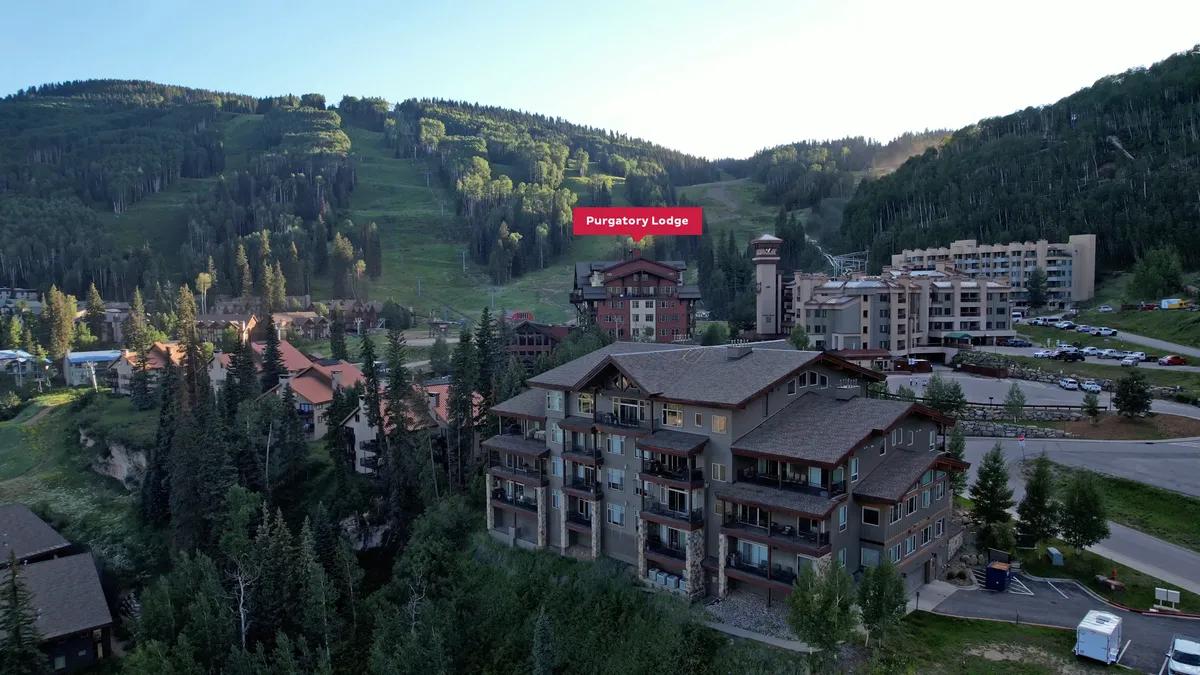 Purgatory Lodge stands among lush greenery, backed by soaring mountains. The exterior scene feels both tranquil and adventurous, highlighting the proximity to nature and all-season activities.
